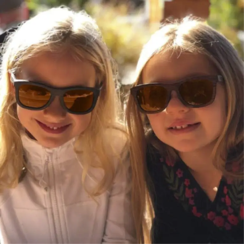 Two children wearing Wildwood sunglasses outdoors with a blurred background